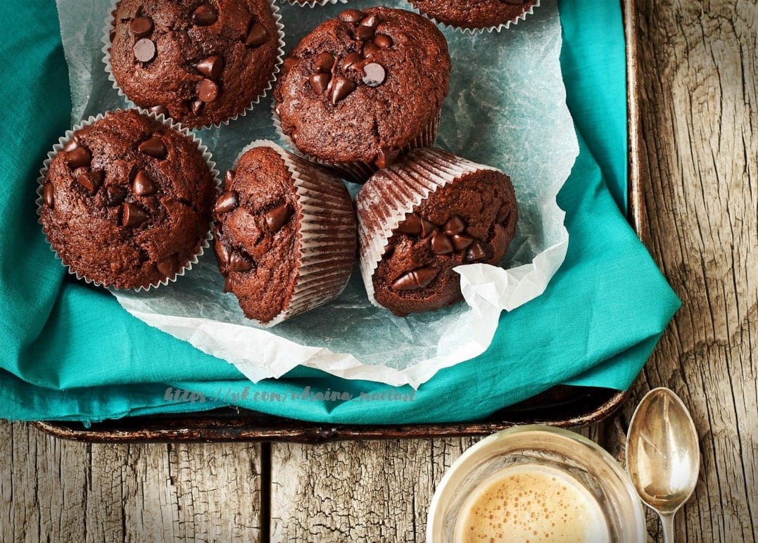 Blech mit Schoko-Chip-Muffins neben einer Tasse Kaffee und einem Löffel