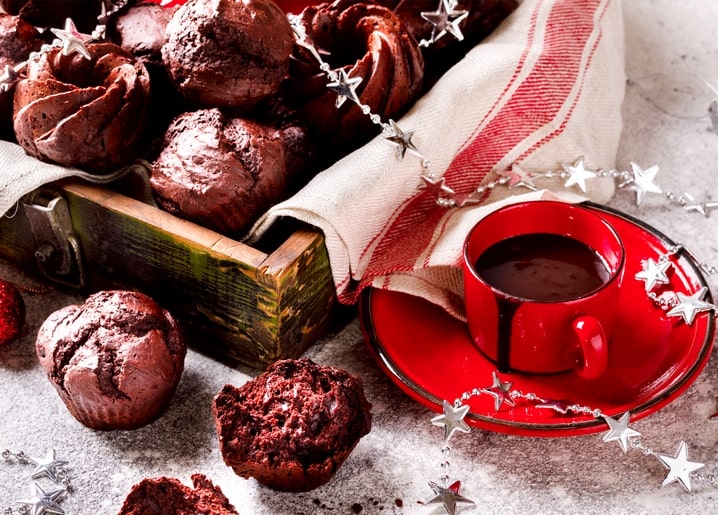 Chocolate muffins in a wooden crate beside a red cup of hot cocoa and silver star garland
