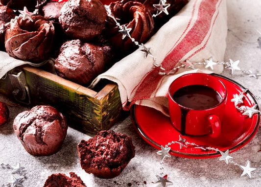 Chocolate muffins in a wooden crate beside a red cup of hot cocoa and silver star garland