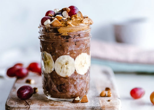 Glas mit Schoko-Overnight-Oats, Bananenscheiben, Trauben und Erdnussbutter