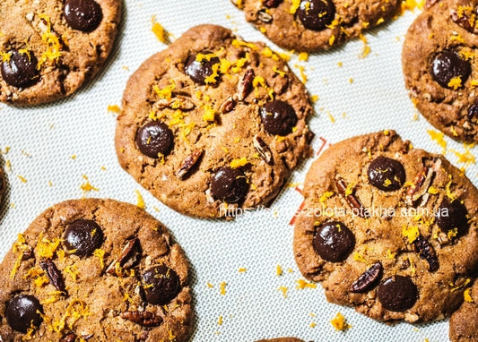 Nahaufnahme von Schoko-Pekan-Keksen mit geriebener Orangenzeste auf einer Backmatte