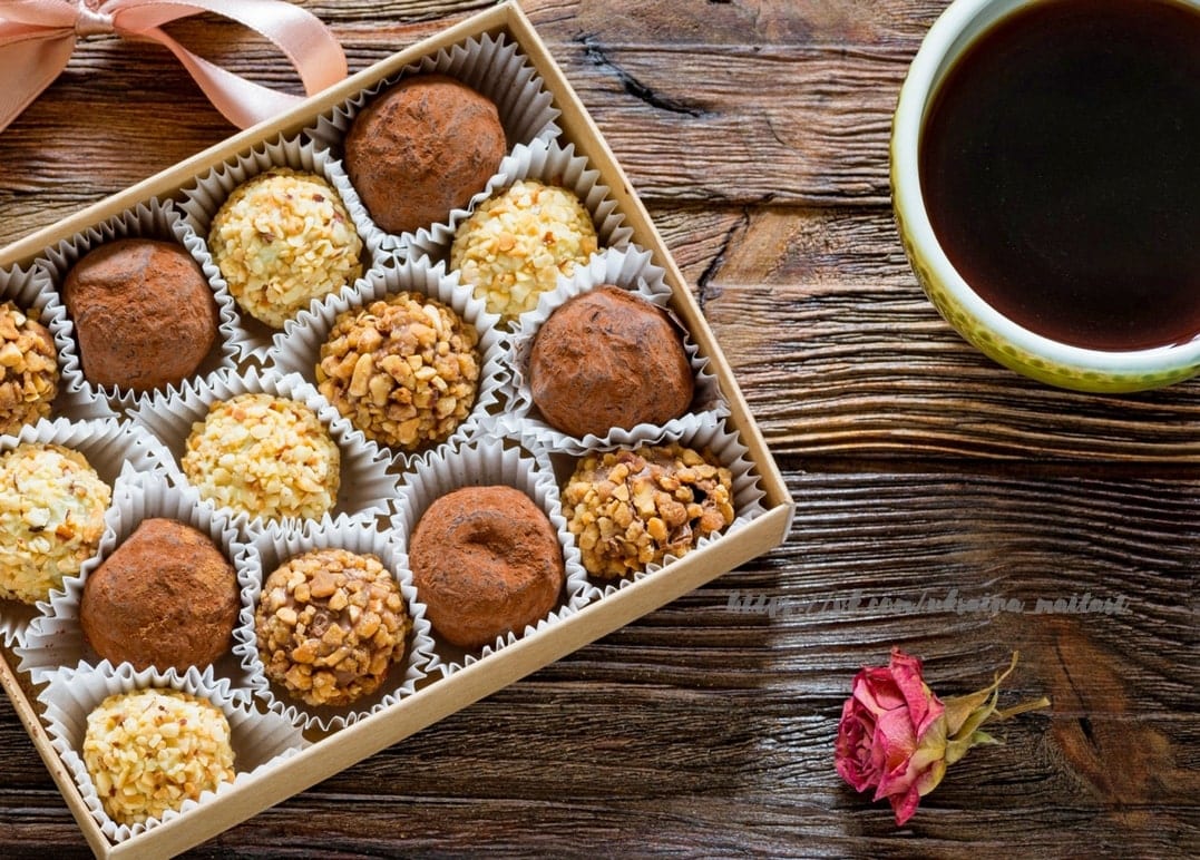 Schachtel Schoko-Trüffel neben einer Tasse Kaffee und einer getrockneten Rose