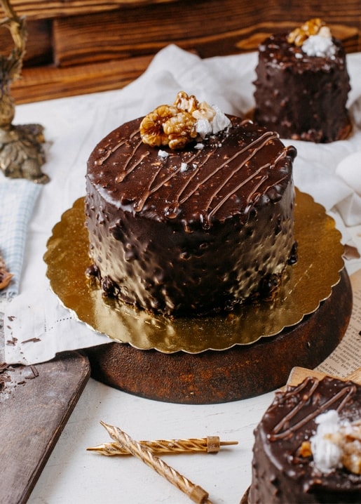 Small chocolate-glazed cake with candied walnuts, gold leaf and birthday candles