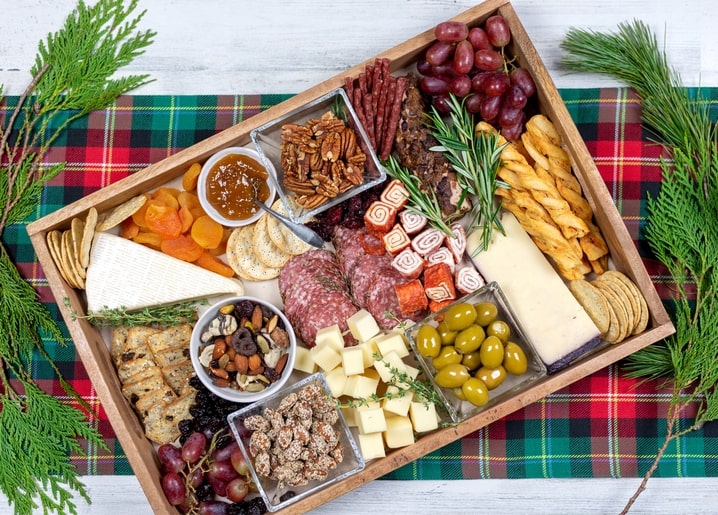 Wooden tray of Christmas charcuterie with cheese, salami, olives, nuts and grapes on tartan cloth