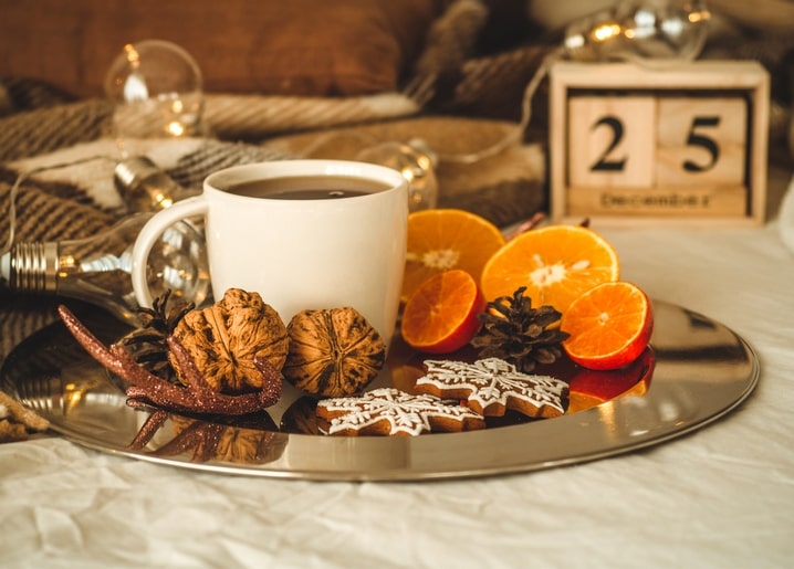Kaffee, Orangenscheiben und Lebkuchensterne neben einem Holzkalender mit dem Datum 25. Dezember