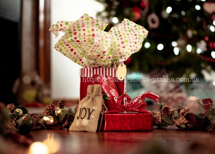 Rote Geschenkbox, Jutesack mit der Aufschrift 'JOY' und gepunktetes Seidenpapier unter dem Weihnachtsbaum