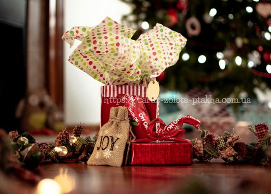 Rote Geschenkbox, Jutesack mit der Aufschrift 'JOY' und gepunktetes Seidenpapier unter dem Weihnachtsbaum