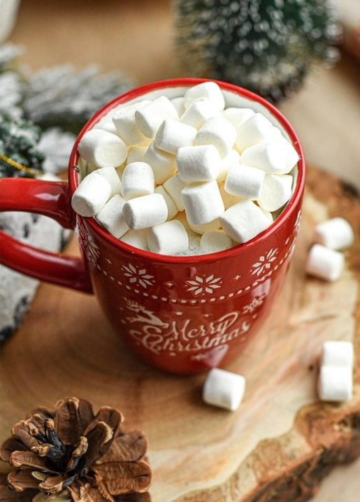 Red Merry Christmas mug filled with marshmallows next to pinecones