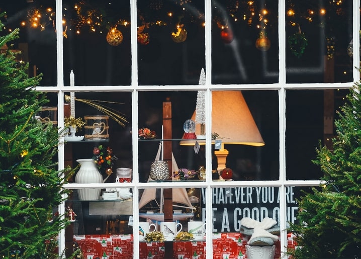 Weihnachtliches Schaufenster mit Lichterkette, Ornamenten und Lampe in der Dämmerung