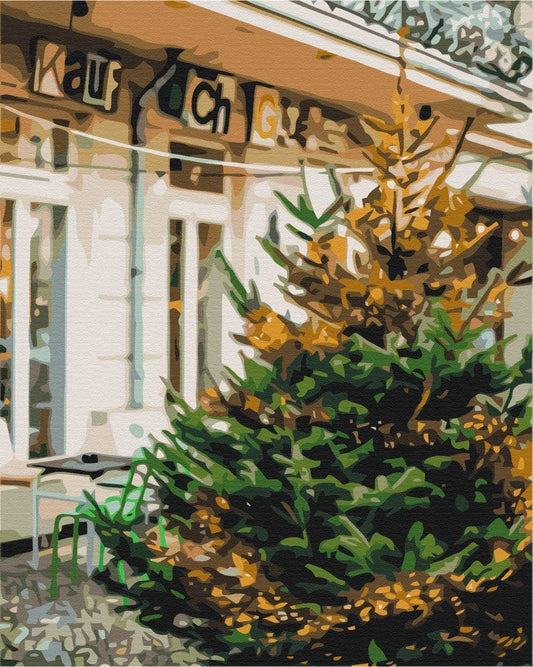 Malen-nach-Zahlen-Motiv: Weihnachtsbaum mit goldenen Lichtern vor einem Café