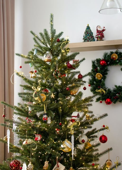 Decorated Christmas tree with fairy lights, baubles, and dried orange slices, wreath in background.
