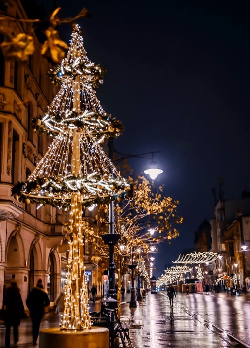 Leuchtender Weihnachtsbaum mit Lichterketten auf nasser Kopfsteinpflasterstraße bei Nacht