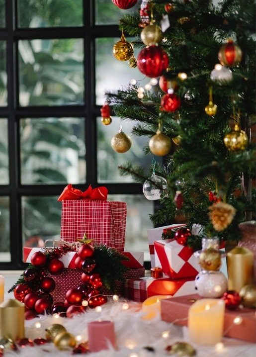 Weihnachtsbaum mit roten und goldenen Kugeln neben Geschenken und brennenden Kerzen