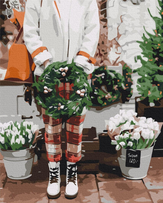 Frau hält Weihnachtskränze neben Eimern mit weißen Tulpen an einem Blumenstand im Freien