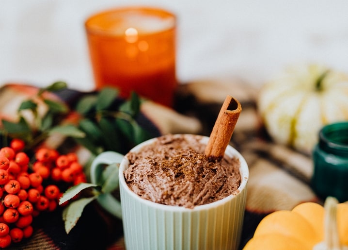 Чашка какао з паличкою кориці біля запаленої свічки та осінніх гарбузів