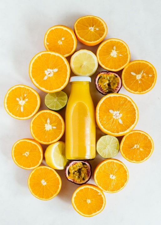 Halbierte Orangen, Zitronen, Limetten und Maracujas um eine Saftflasche, Draufsicht