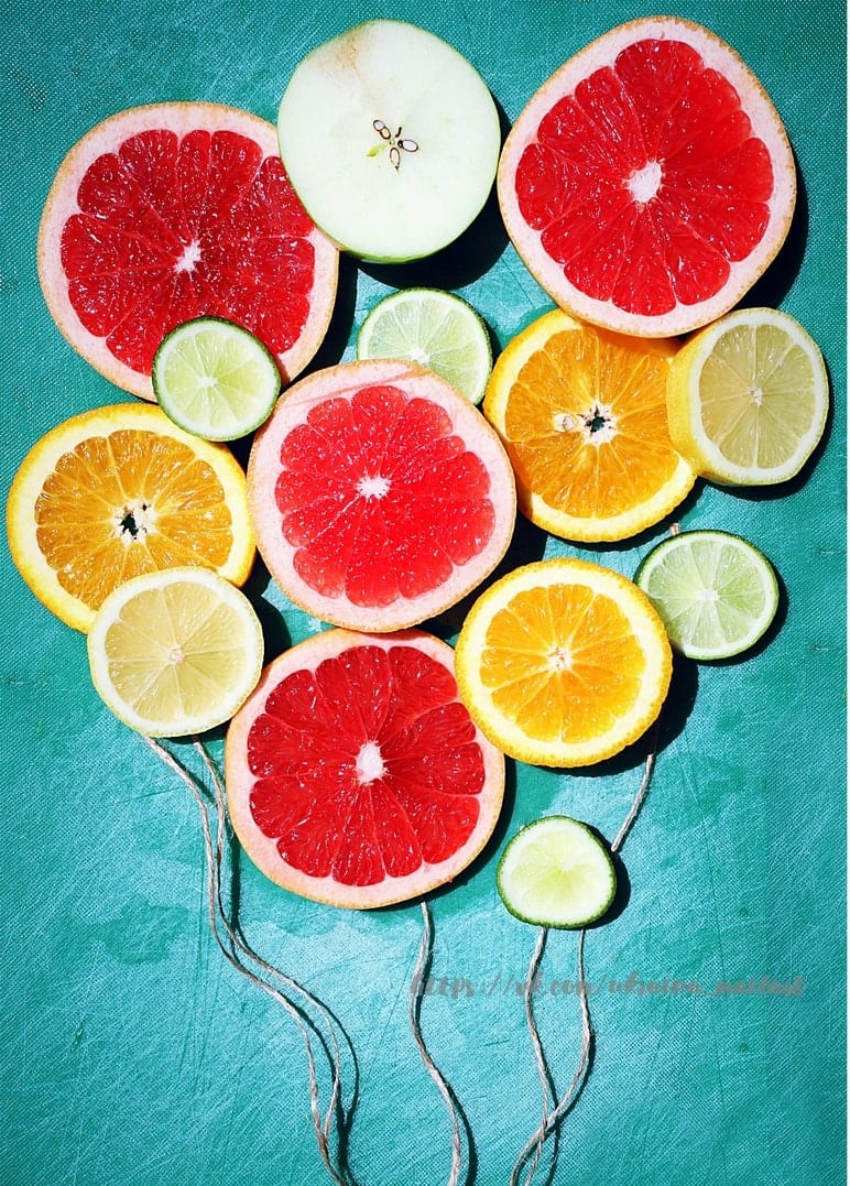 Grapefruit, orange, lemon, lime and apple slices arranged like balloons on strings on teal