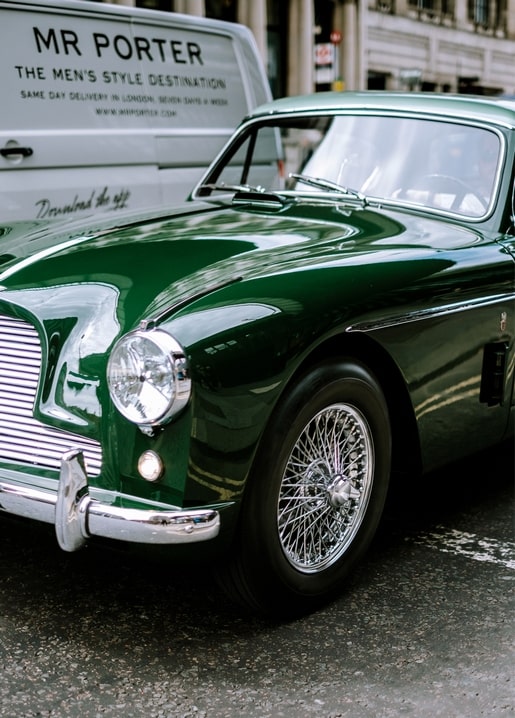 Nahaufnahme eines dunkelgrünen Oldtimer-Sportwagens mit verchromten Drahtspeichenrädern auf einer Stadtstraße