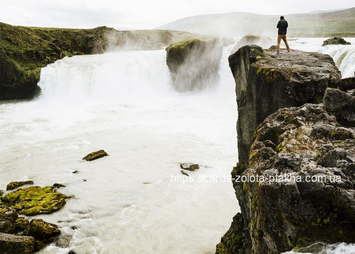 Wanderer steht auf einer Klippe über einem breiten, nebligen Wasserfall