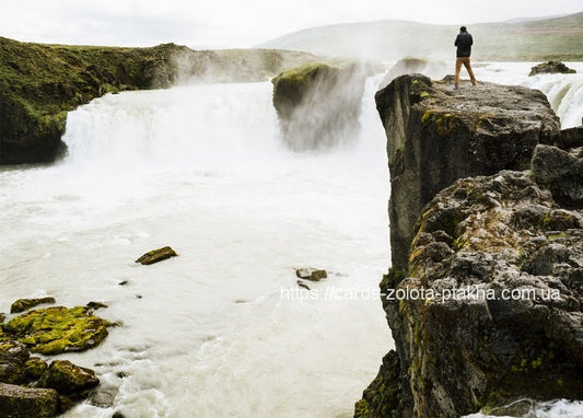 Wanderer steht auf einer Klippe über einem breiten, nebligen Wasserfall