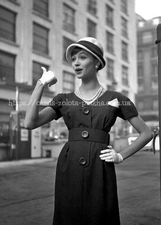 Schwarzweißfoto aus den 1950ern: Frau mit Cloche-Hut und Perlenkette winkt ein Taxi auf der Straße
