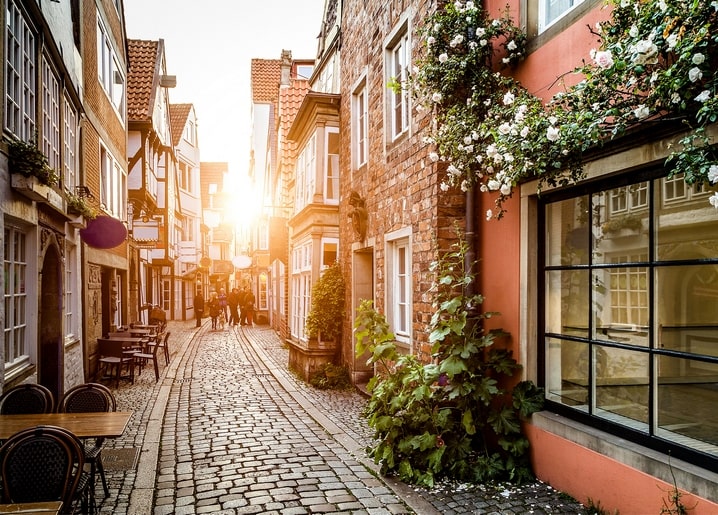 Kopfsteinpflastergasse einer Altstadt mit weißen Kletterrosen bei Sonnenuntergang