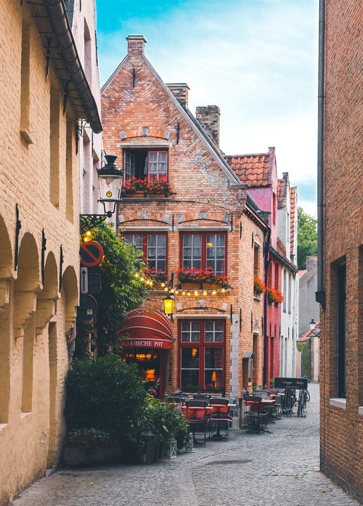 Kopfsteinpflastergasse mit beleuchtetem Café, Lichterkette und Blumenkästen