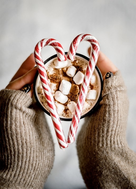 Hands in a sweater holding cocoa framed by a candy-cane heart