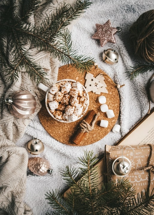 Overhead flat lay of cocoa, pine branches, ornaments and a wrapped gift
