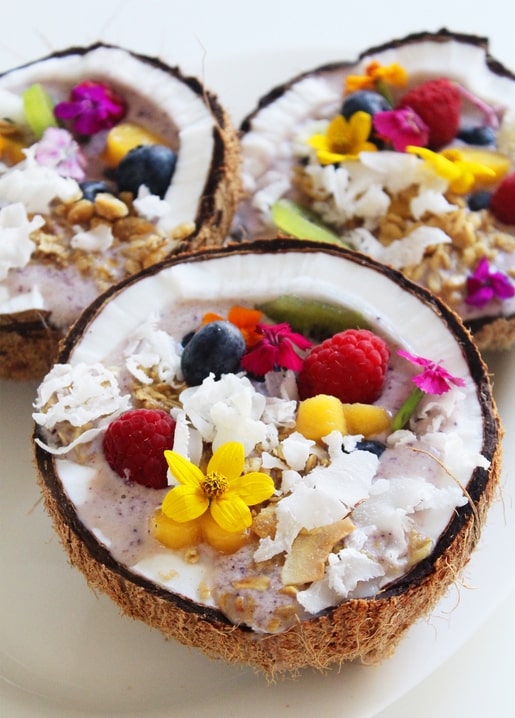 Kokosnussschalen mit Beeren-Smoothie, Granola und essbaren Blüten