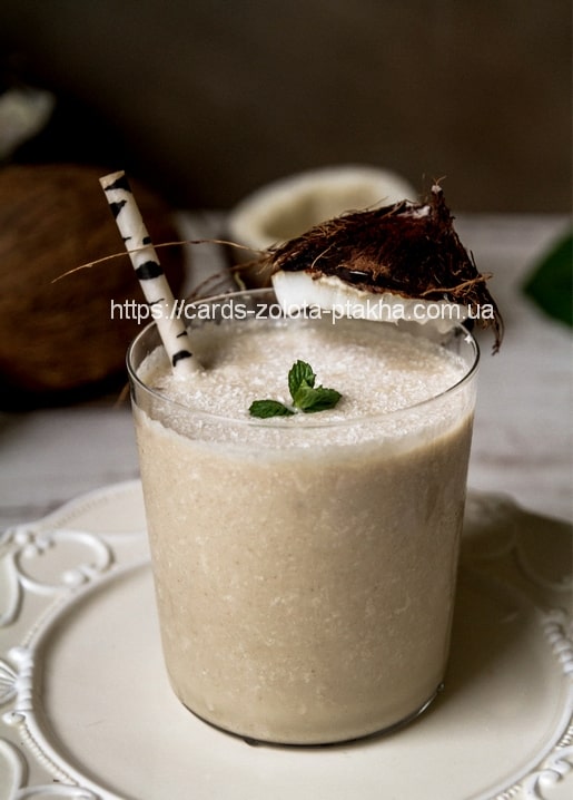 Kokosnuss-Smoothie im Glas mit gestreiftem Strohhalm, Minze und Kokosnussschale
