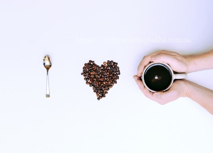 Herz aus Kaffeebohnen, Löffel und Hände mit einer Tasse auf weißem Hintergrund