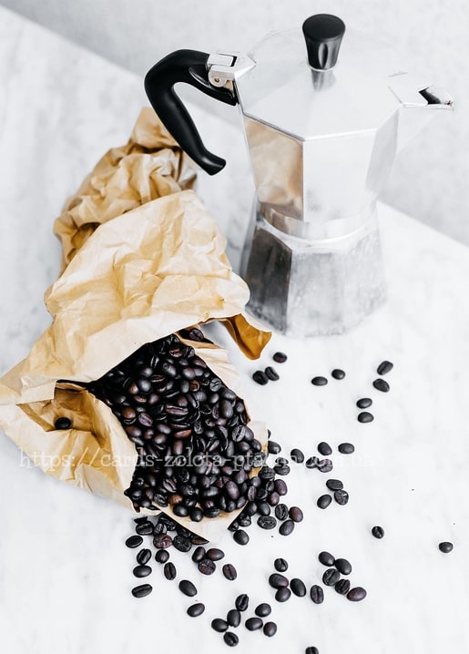 Kaffeebohnen fallen aus einer Papiertüte neben einem Espressokocher auf Marmor