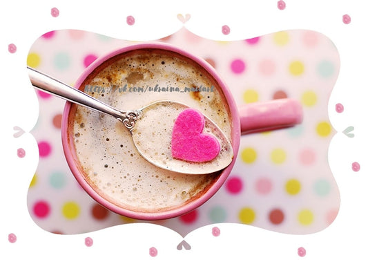 Schaumiger Kaffee in rosa Tasse mit silbernem Löffel und rosa Filzherz, gepunkteter Hintergrund