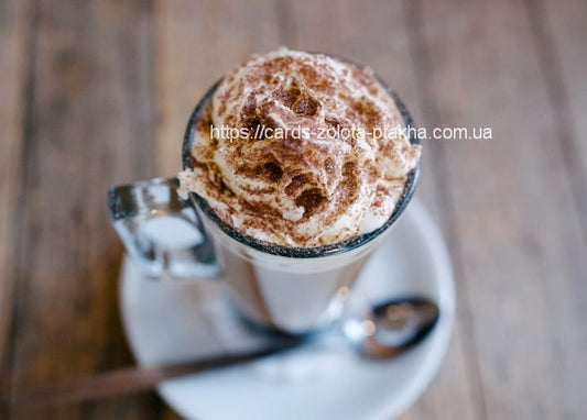 Glas Kaffee mit Schlagsahne und Kakaopulver, Löffel und Untertasse auf Holztisch