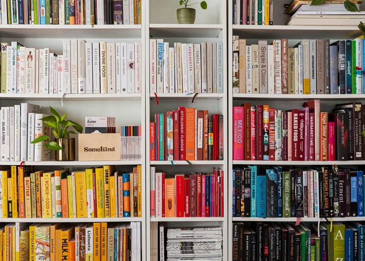 Барвиста книжкова полиця з кулінарними книгами, рослинами та кухонним декором