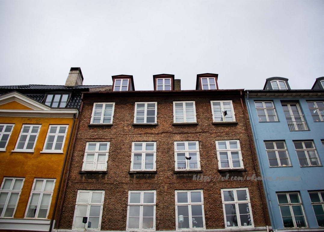 Reihe aus gelben, ziegelroten und blauen Hausfassaden unter schwarzen Dächern mit Dachgauben