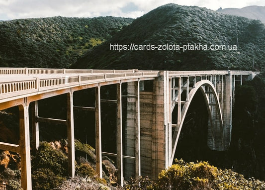 Helle Betonbogenbrücke entlang grüner, sonniger Küstenhügel