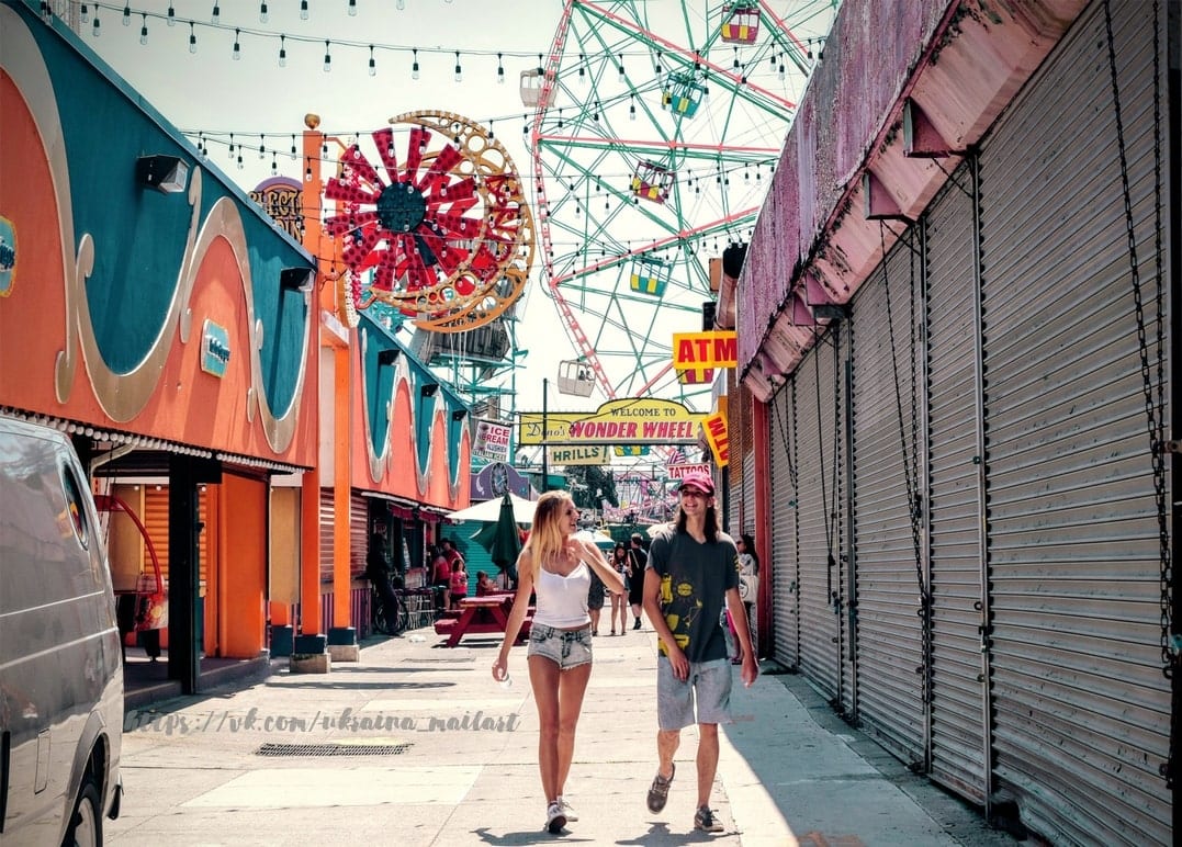 Bunte Strandpromenade auf Coney Island mit Riesenrad-Schild und schlenderndem Paar