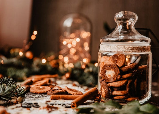 Glass jar of gingerbread cookies with cinnamon sticks, pine, and fairy lights blurred behind