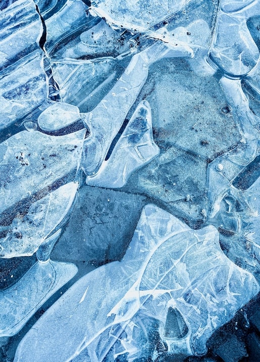 Nahaufnahme von rissigem blauem Seeeis mit Frostmustern und hellen Brüchen