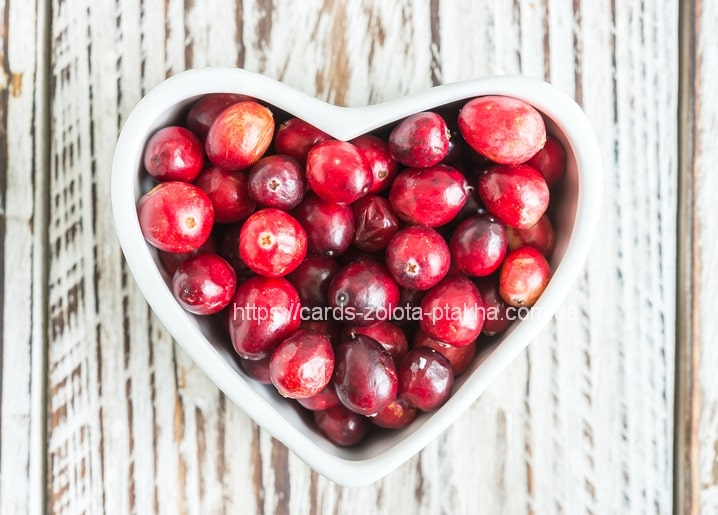 Herzförmige weiße Schale mit glänzenden roten Cranberries auf hellem Holz