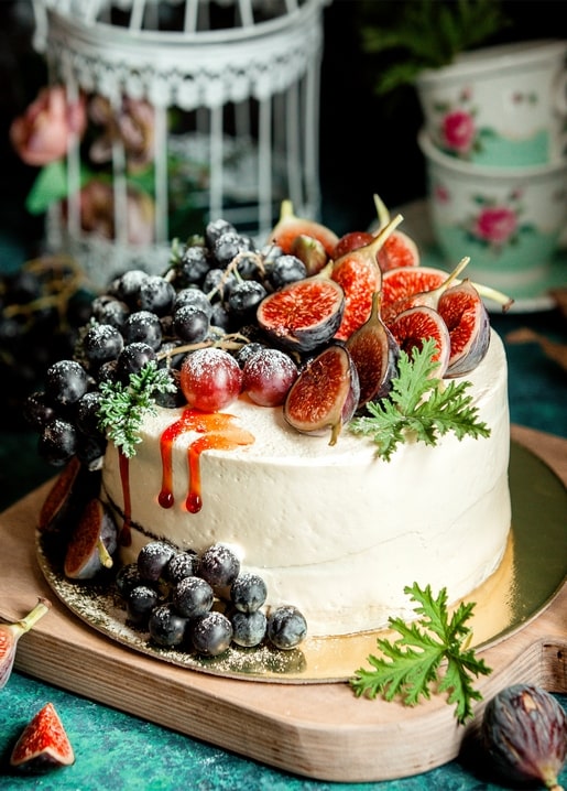 Sahnetorte mit Feigen, schwarzen und roten Trauben und Honig neben einem Vogelkäfig