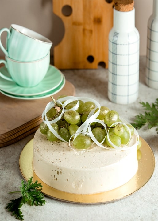 Sahnetorte mit grünen Trauben neben mintgrünen Teetassen und karierten Flaschen