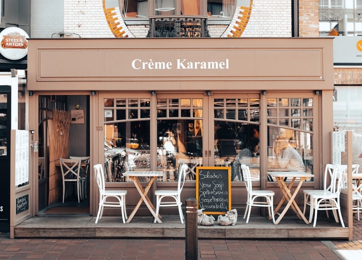 Рожевий фасад кафе Crème Karamel з вуличними столиками та стільцями