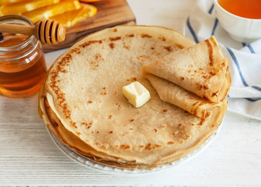 Стос тонких млинців з маслом, банкою меду та скибочками апельсина