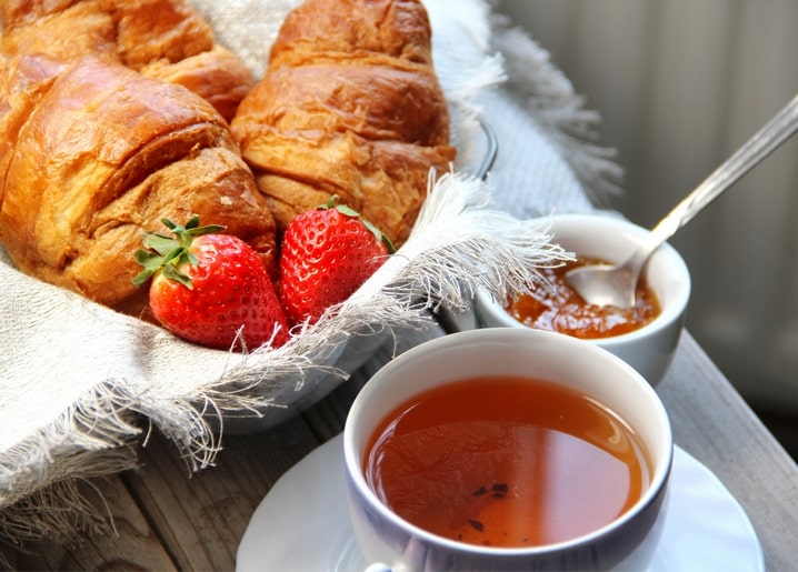 Postkarte mit Croissants, Erdbeeren, Marmelade und Tee auf einem Holztisch