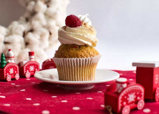 Cupcake with cream swirl and raspberry beside a red wooden toy train on polka-dot cloth