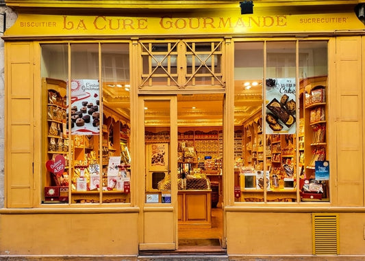 Gelbes Schaufenster der Konditorei La Cure Gourmande in der Abenddämmerung