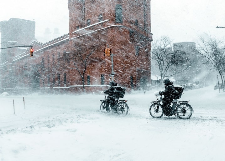 Zwei Radfahrer fahren durch dichten Schnee an einem Backsteinturm vorbei